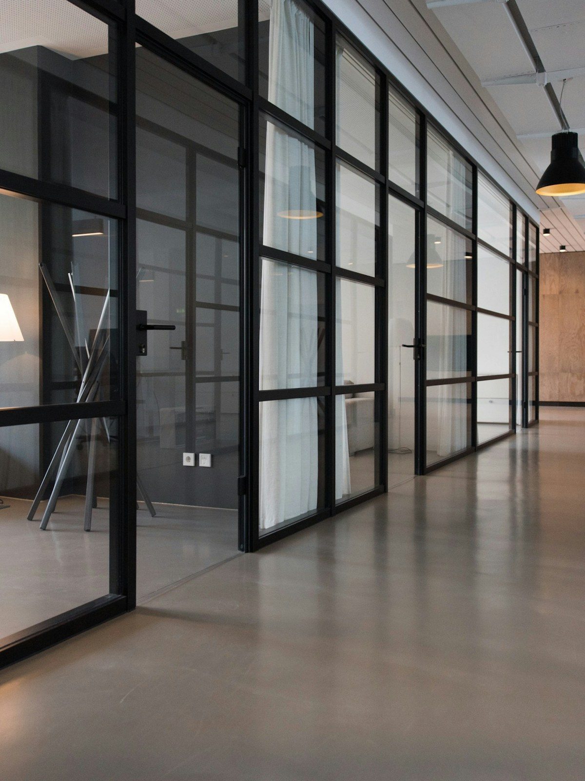 Office corridor with black-framed glass partitions and a polished concrete floor